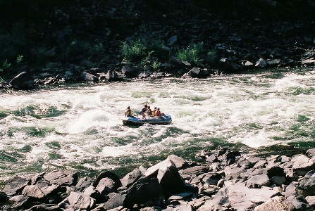 [About a half dozen people are in a large inflatable raft on a wide river with lots of whitewash and rapids. It looks to be a very bumpy ride.]